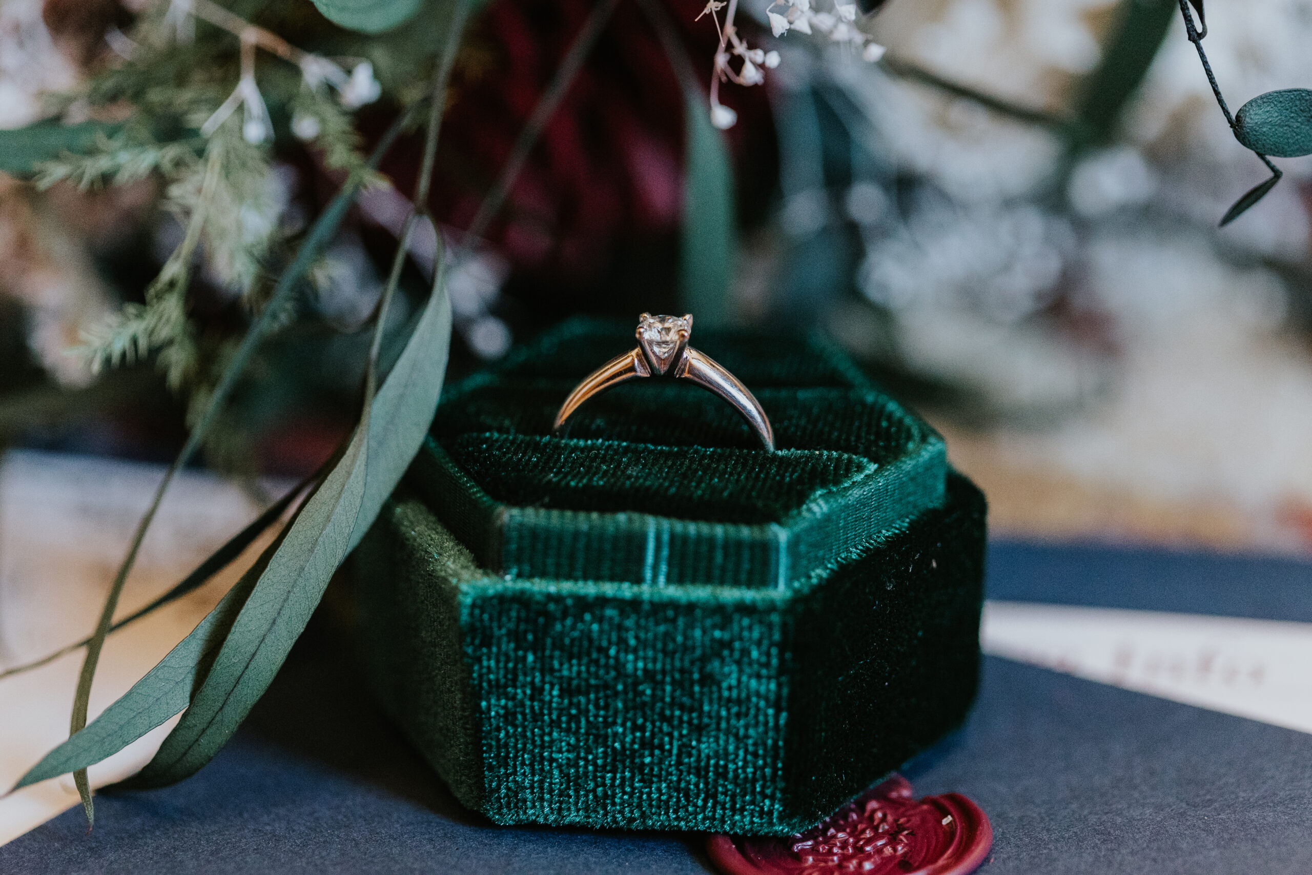 macro shot of a wedding ring in a box surrounded by wedding floral arrangements